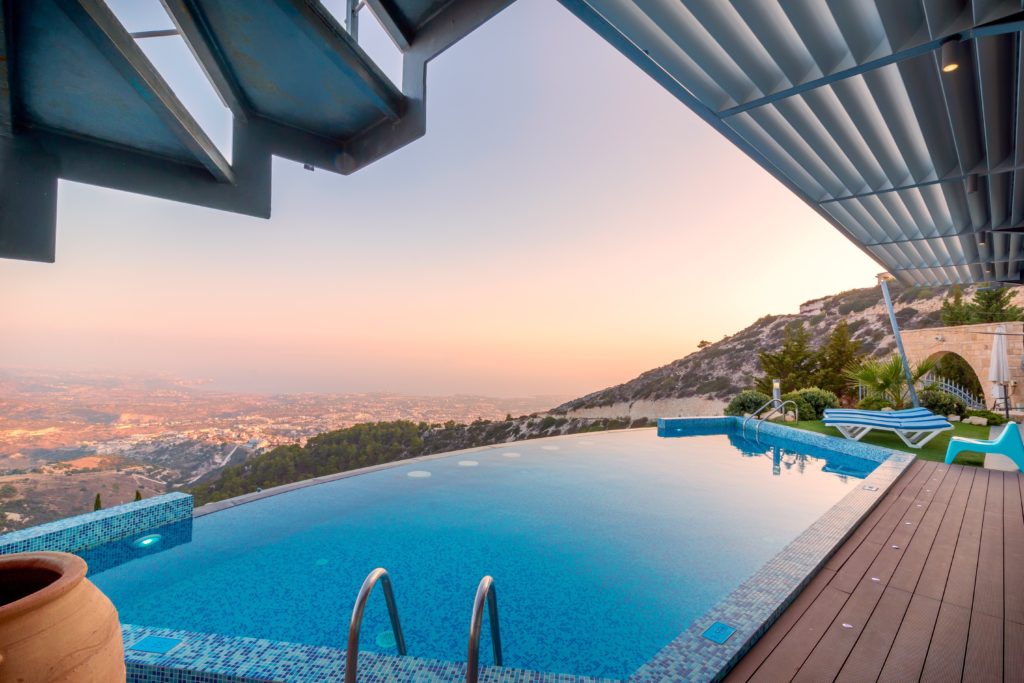 Sun loungers by infinity pool in Greek villa at sunset.