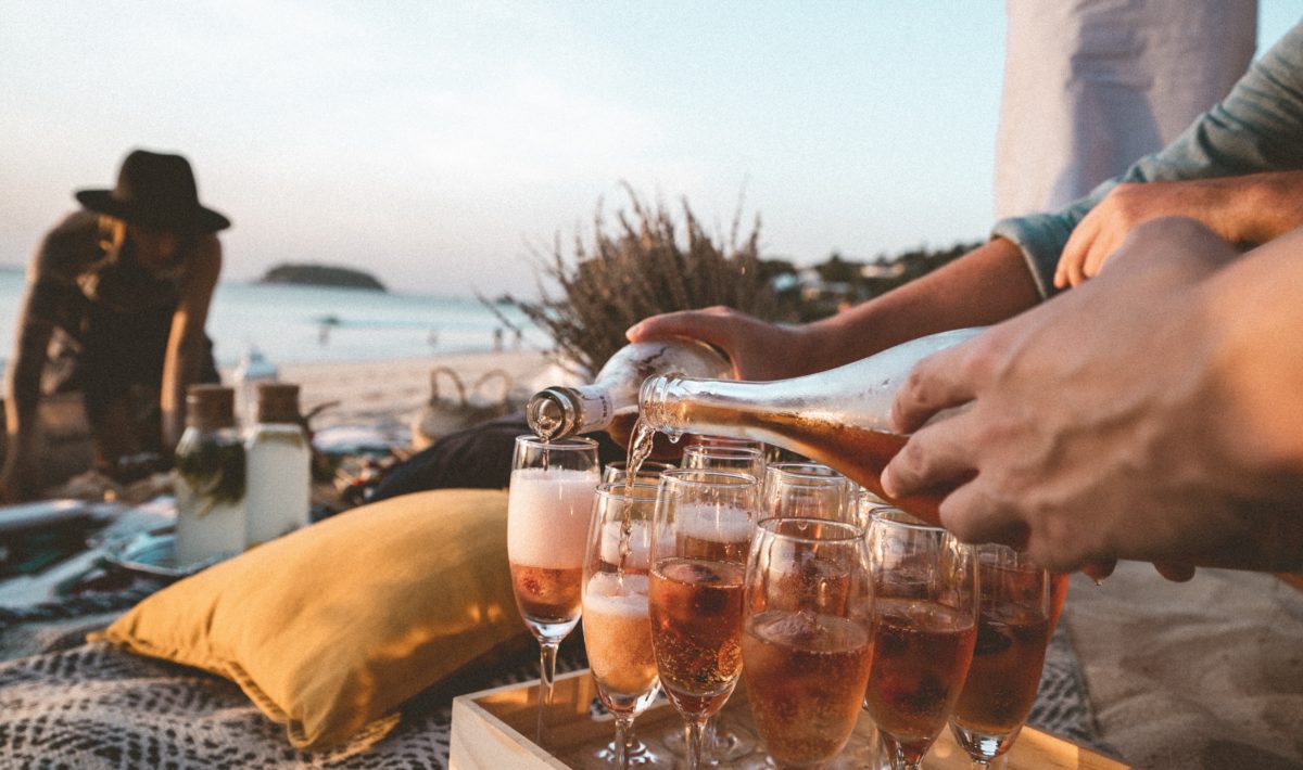 Pink sparkling wine being poured into flute glasses on the beach at one of the best Greek islands for partying.