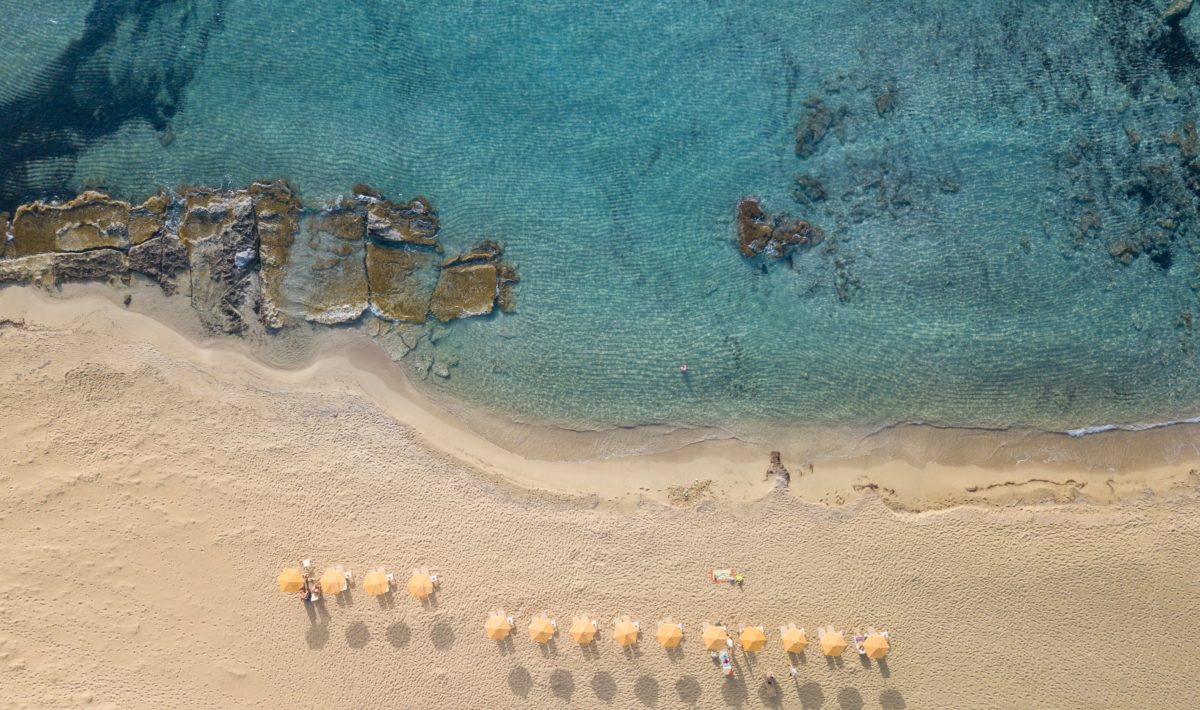 A bird's eye perspective of a family friendly Greek island beach with yellow parasols and sunbeds.