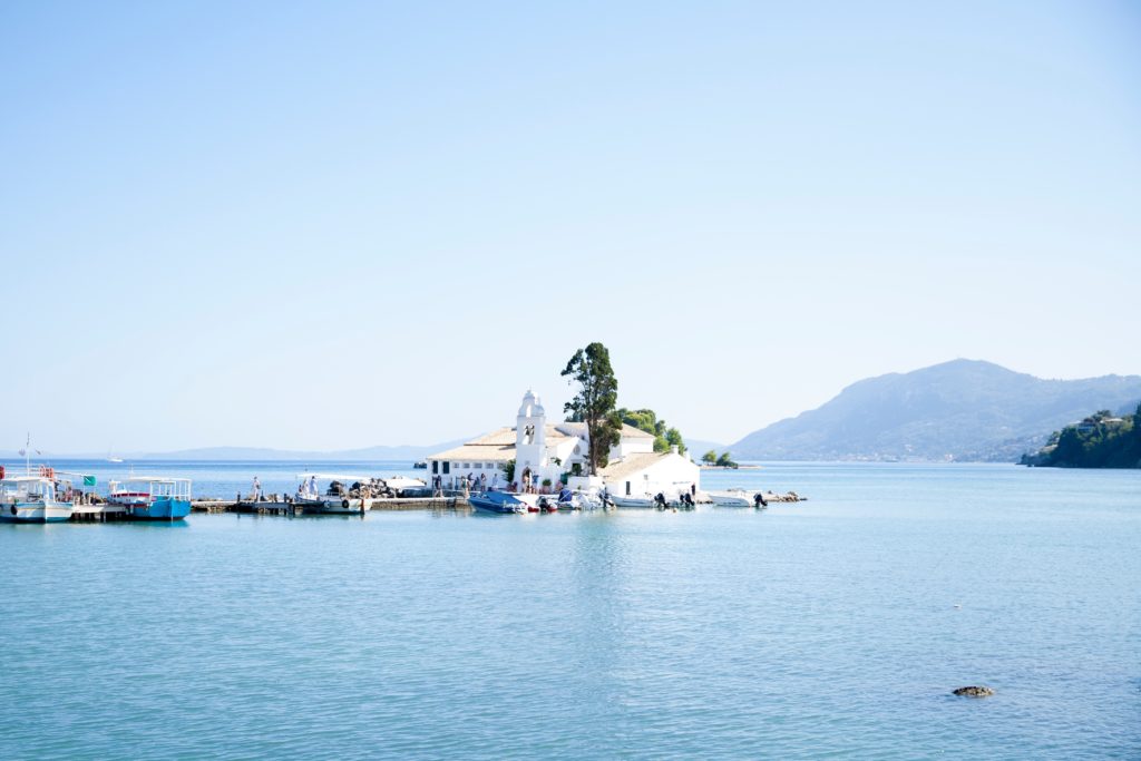 Surrounded by blue sky and sea is a whitewashed Greek building at the end of a pontoon.