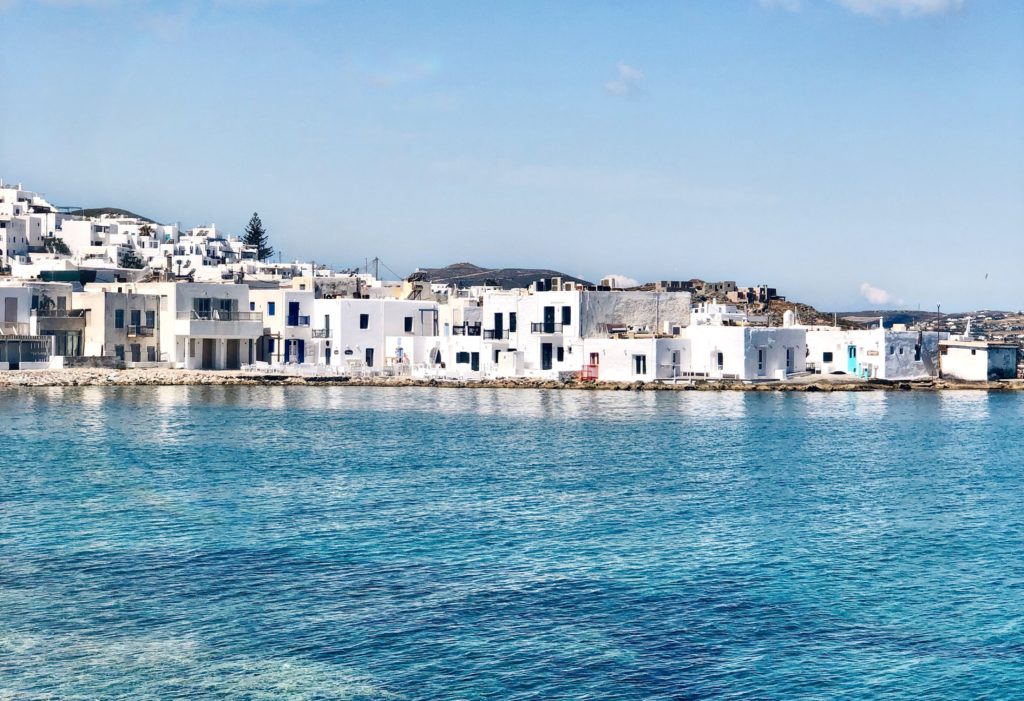 whitewashed houses contrast with shallow blue waters and clear blue sky at one of the best Greek islands for families.